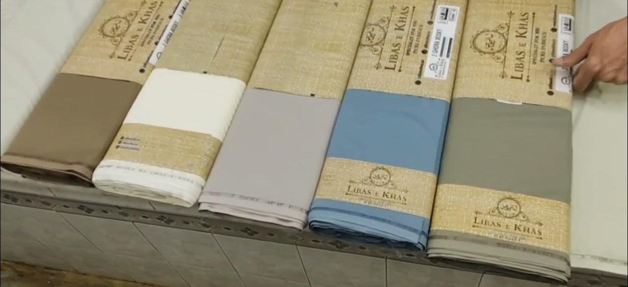 Rolls of fabric with 'Lekas & Kral' branding on a wooden surface.